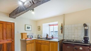 A kitchen with wooden cabinets, a stove, and a window with a red frame. - 3 Bed in Cumbria (oc-sz101) (Crosthwaite and Lyth)