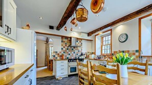 Uma cozinha com painel de azulejos, cadeiras de madeira, uma mesa de jantar e um relógio na parede.