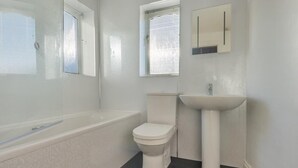 Et badeværelse med badekar, toilet og et håndvaskskab.