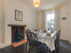 A dining area with a table set for four, a wood-burning stove, and a window with curtains. - 3 Bed in Keswick (oc-sz187) (Keswick)