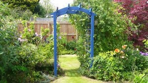Un vialetto fiorito con un arco blu, circondato da diverse piante e fiori.