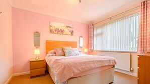 Una camera da letto con un letto, comodini, una finestra con persiane, un termosifone e un quadro appeso al muro.