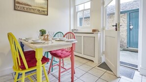 A dining area with a table set for four, colorful chairs, a window with blinds, and a door leading outside. - 2 Bed in Keswick (oc-sz009) (Keswick)
