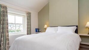 A neatly made bed with white linens, a window with curtains, and two bedside lamps. - 2 Bed in Keswick (oc-sz009) (Keswick)