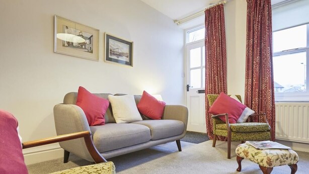 A living room with a sofa, armchairs, a patterned ottoman, and a window with curtains. - 2 Bed in Keswick (oc-sz009) (Keswick)