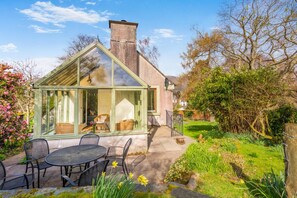 A conservatory with a glass roof, a patio with outdoor seating, and a garden with flowering plants. - 3 Bed in Keswick (oc-sz142) (Portinscale)