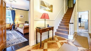 A hallway with a checkered floor, a staircase, a dining area with a table and chairs, and a view into a kitchen. - 5 Bed in Keswick (oc-sz359) (Keswick)