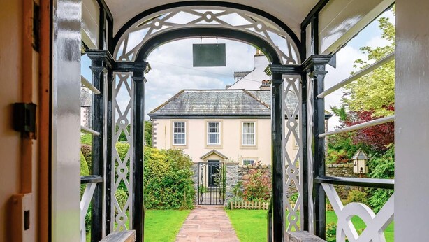 A covered walkway leading to a house with a stone pathway, white fence, and a gate. - 5 Bed in Keswick (oc-sz359) (Keswick)