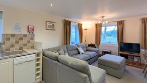 A compact living space with a sofa, ottoman, TV, and a kitchenette. - 3 Bed in Keswick (oc-sz508) (Stair)