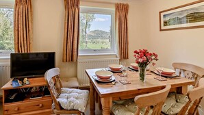 A dining area with a table set for four, a television on a wooden stand, and a window with curtains. - 3 Bed in Keswick (oc-sz508) (Stair)
