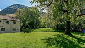 A grassy yard with a picnic table, a swing set, and a building with windows. - 3 Bed in Keswick (oc-sz508) (Stair)