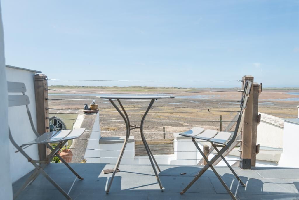 En balkong med ett bord och två stolar, med utsikt över en strand.