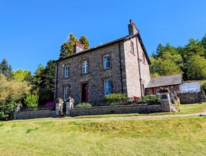 A stone building with a red door, multiple windows, and a stone wall in front. - 8 Bed in Holmrook (oc-sz182) (Boot)