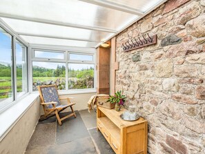 A conservatory with a stone wall, a wooden bench, a chair, and a view of the outdoors. - 8 Bed in Holmrook (oc-sz182) (Boot)