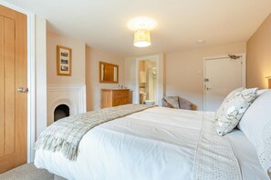 A bedroom with a bed, a dresser, a mirror, a door, and a fireplace.