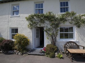 A white building with a door, windows, and a wooden bench outside. - 3 Bed in Keswick (oc-sz075) (Borrowdale)