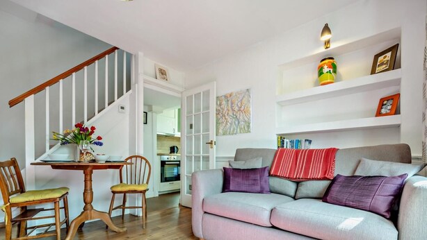 A living room with a sofa, chairs, a dining table, and a staircase. - 1 Bed in Keswick (oc-sz472) (Keswick)