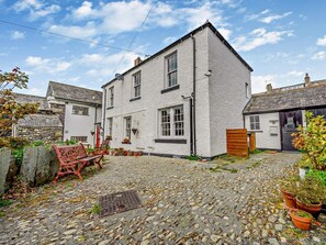 A two-story house with a stone-paved courtyard, a red bench, and potted plants. - 1 Bed in Keswick (oc-sz472) (Keswick)