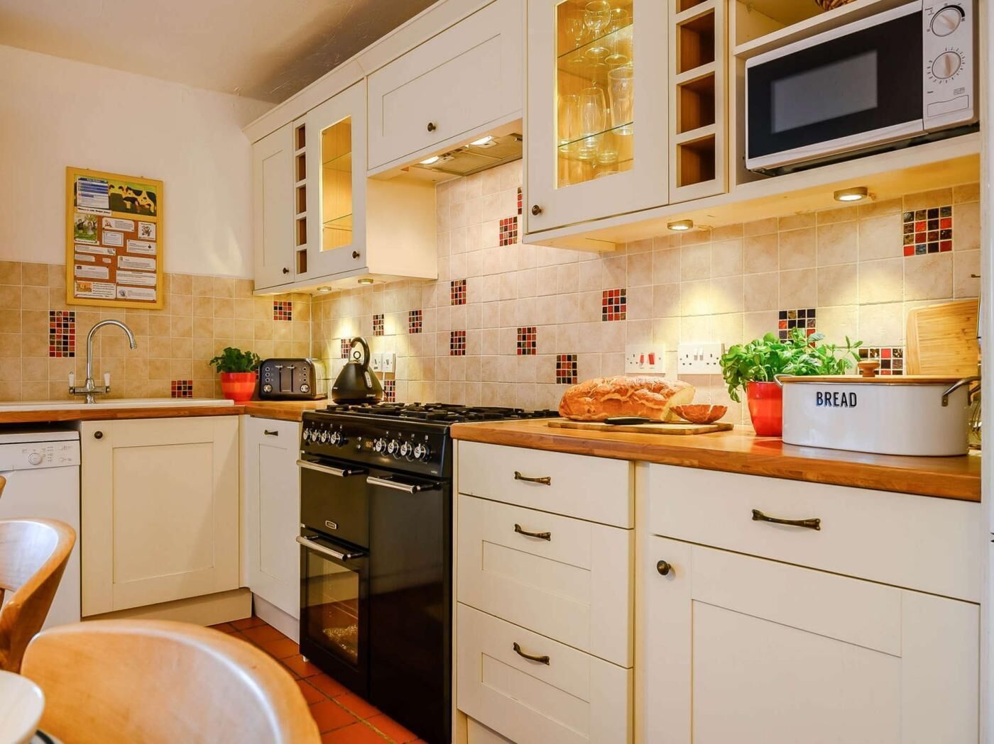 A kitchen with white cabinets, a stove, a microwave, and a bread container.