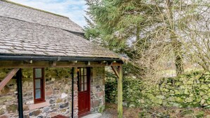A stone cottage with a thatched roof, a wooden bench, and a stone wall. - 2 Bed in Penrith (oc-sz339) (Ullswater)