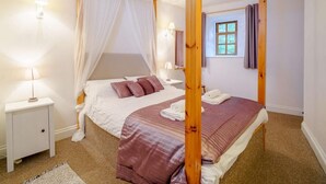A four-poster bed with a canopy, a bedside table with a lamp, a window with curtains, and a small stool. - 2 Bed in Penrith (oc-sz339) (Ullswater)