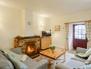 A cozy living room with a stone fireplace, a television on a wooden cabinet, and a window with curtains. - 2 Bed in Penrith (oc-sz339) (Ullswater)