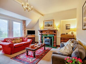 Ein Wohnzimmer mit Kamin, einem roten Sofa, einem grauen Sessel und einem Fernseher.
