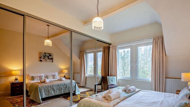 Een slaapkamer met een grote spiegel, twee bedden, een kroonluchter en uitzicht op het landschap.