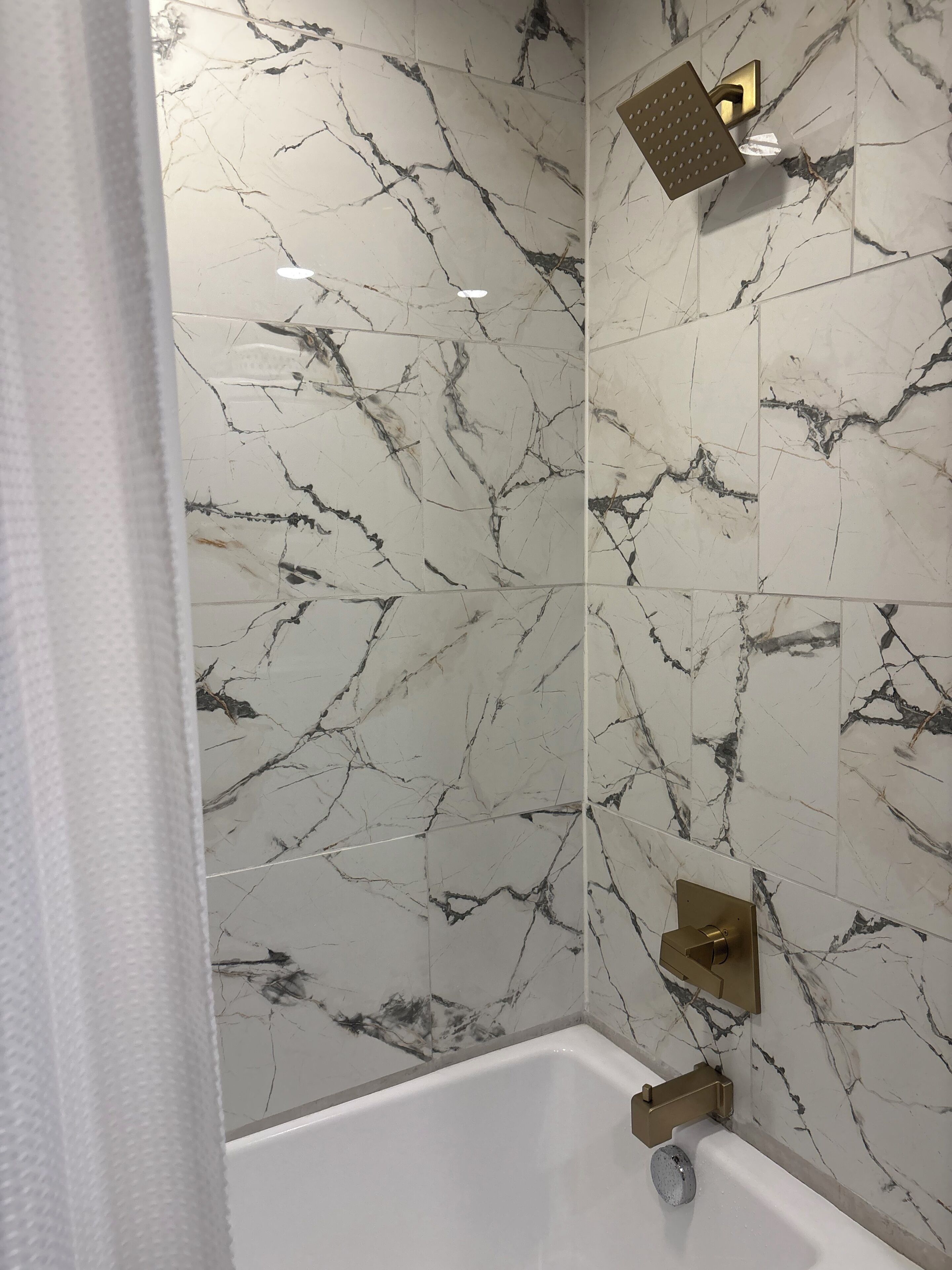 A bathroom with a bathtub, a showerhead, and marble-patterned walls.
