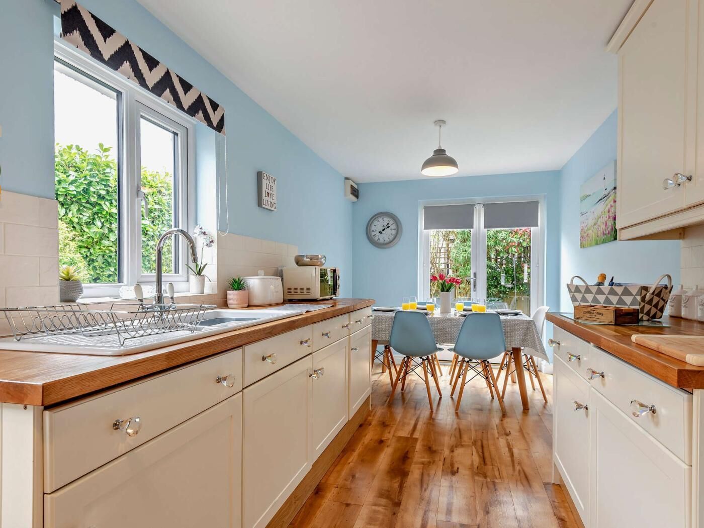 Une cuisine avec un plan de travail en bois, un évier, une table à manger avec des chaises et une vue sur la verdure à l’extérieur.