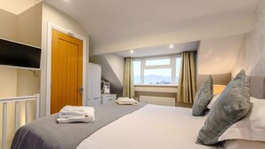 A hotel room with a bed, a television, a wardrobe, a window with curtains, and a view of the outside. - 2 Bed in Keswick (oc-sz036) (Keswick)