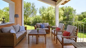 A covered patio with wicker furniture, a table, and a view of greenery. - Villa in Son Servera With Private Pool & Beaches (Son Servera)