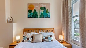 A bedroom with a wooden headboard, a bed with white bedding, two bedside lamps, and a window with curtains. - 2 Bed in Keswick (oc-sz026) (Keswick)