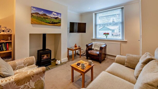 A living room with a fireplace, a sofa, a coffee table, a bookshelf, and a painting of a landscape. - 2 Bed in Keswick (oc-sz026) (Keswick)