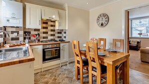 A modern kitchen with a dining area, featuring a stove, oven, and a clock on the wall. - 2 Bed in Keswick (oc-sz026) (Keswick)