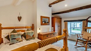 Quarto com cama de madeira, cômoda, cadeira de balanço, espelho e janela com vista.