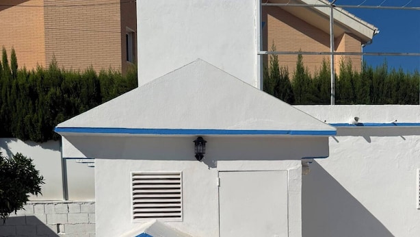 Een wit gebouw met een blauw dak, een kleine deur en een raam.