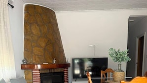 Een woonkamer met een stenen open haard, een flatscreen televisie, een eettafel met stoelen en een bank.