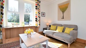A living room with a sofa, a table with a vase of flowers, a lamp, and a painting on the wall. - 2 Bed in Ravenglass (oc-sz514) (Ravenglass)