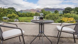 A patio with two chairs and a table, overlooking a scenic landscape with mountains and greenery. - 3 Bed in Keswick (oc-sz528) (Portinscale)