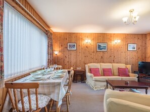Ein Essbereich mit Tisch für vier Personen, einer Couch, einem Fernseher und gerahmten Bildern an der Wand.