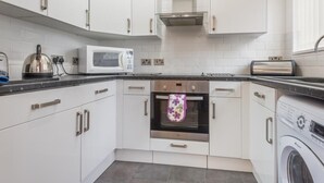 A modern kitchen with white cabinets, a microwave, an oven, and a washing machine. - 2 Bed in Cockermouth (oc-sz164) (Mockerkin)