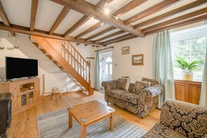 A living room with a wooden staircase, a sofa, a coffee table, and a television on a wooden cabinet. - 2 Bed in Penrith (oc-sz276) (Stainton)