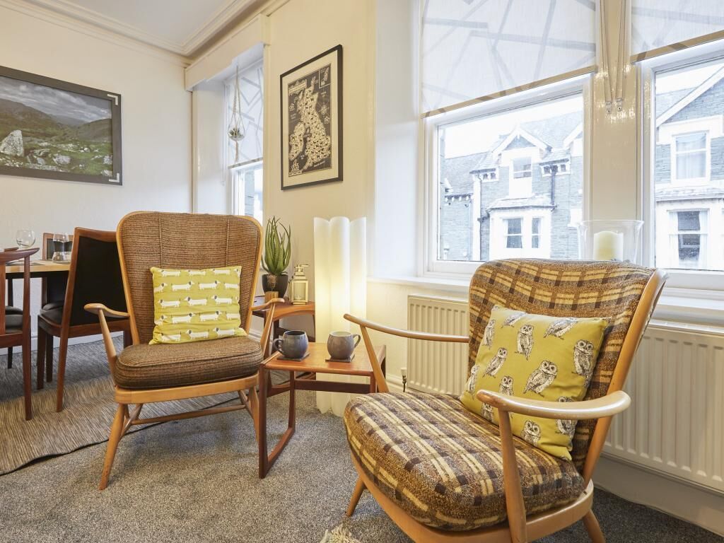 Ein gemütliches Zimmer mit zwei Korbstühlen, einem kleinen Tisch und einem Fenster mit Blick auf Gebäude.