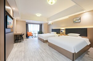 Una habitación de hotel con dos camas, un escritorio, una silla, un televisor y un ventanal con cortinas.