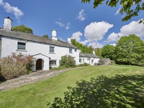 A white building with a stone pathway leading to the entrance, surrounded by greenery and trees. - 5 Bed in Holmrook (oc-sz259) (Eskdale)
