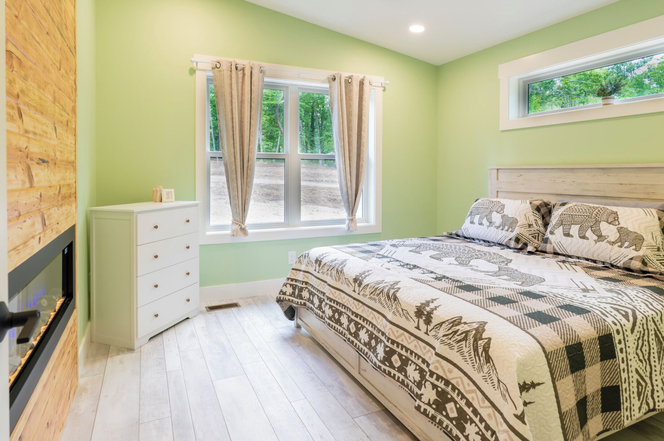 A bedroom with a bed, a window with curtains, a dresser, and a fireplace.