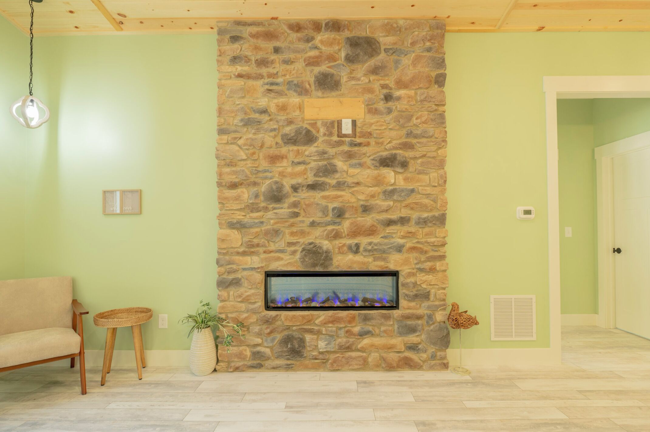 Een stenen openhaard met glazen deur, een houten plafond, een groene wand en een betegelde vloer.