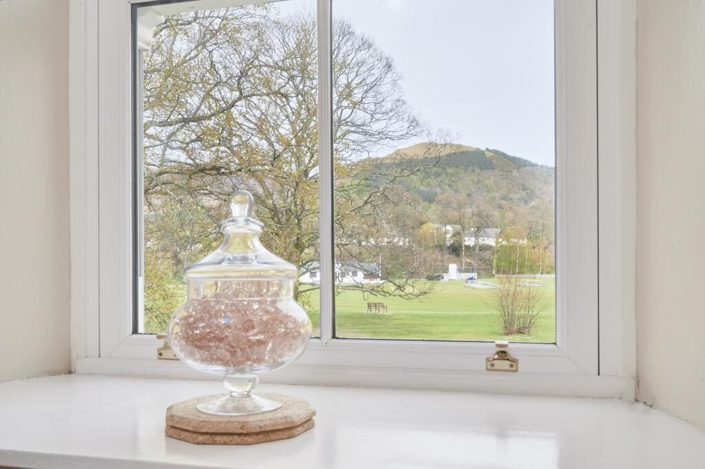 A clear view of a window with a glass jar on a coaster, a white window frame, and a landscape view of trees and hills.