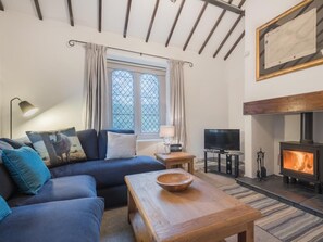 Ein gemütliches Wohnzimmer mit einer Couch, einem Couchtisch, einem Fernseher, einem Kamin und einem Fenster mit Vorhängen.